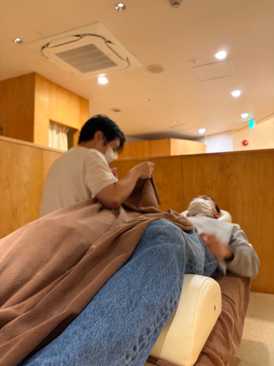 とんとん整骨院の練習会で、ベッドに仰向けになった受け役のスタッフにタオルをかけて施術の手順を確認するスタッフ
