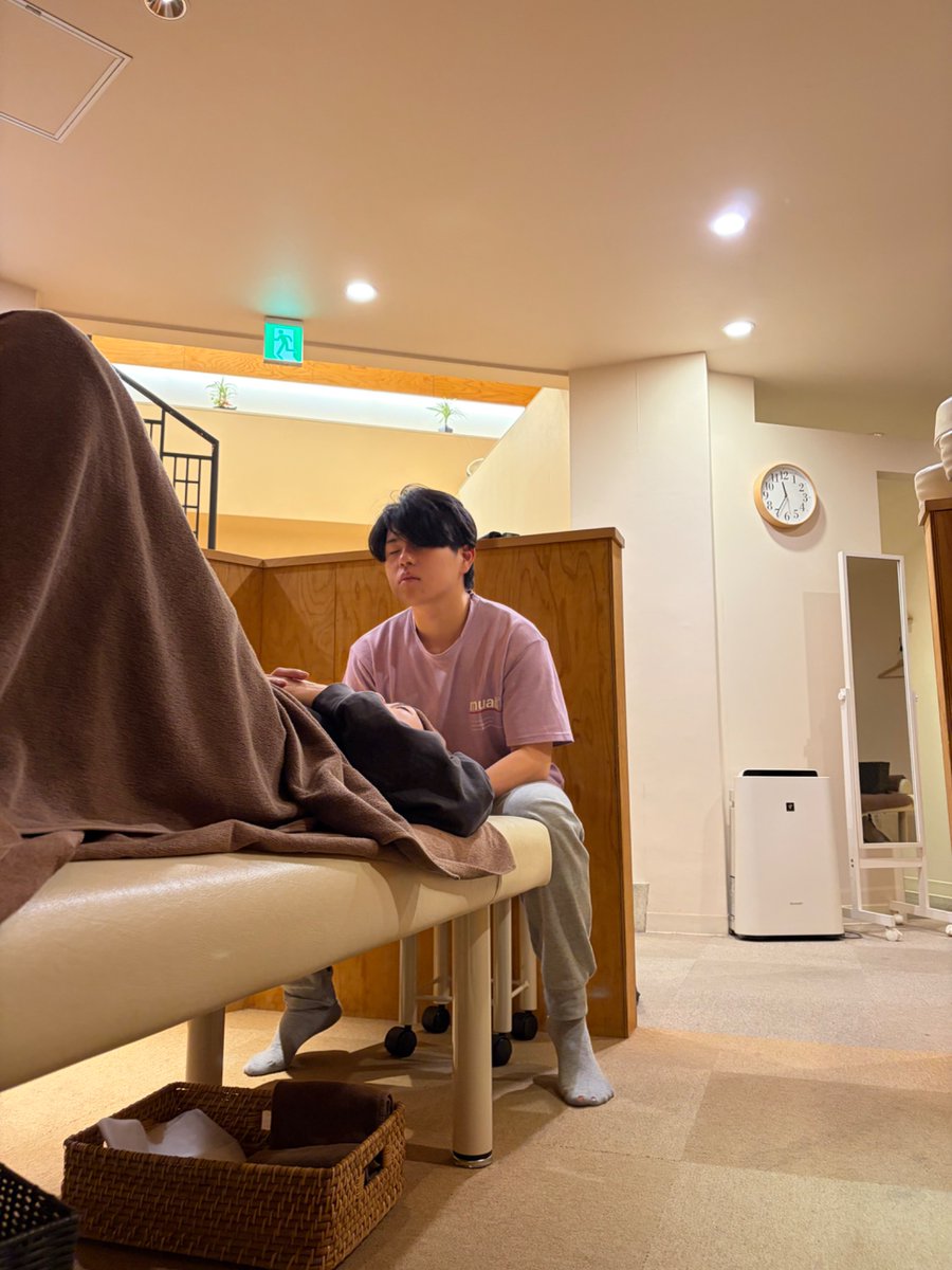 とんとん整骨院の練習会で、腕を胸の前で組んで立った受け役のスタッフの骨盤に両手を当て、しゃがんだ姿勢で動きを確かめるスタッフ