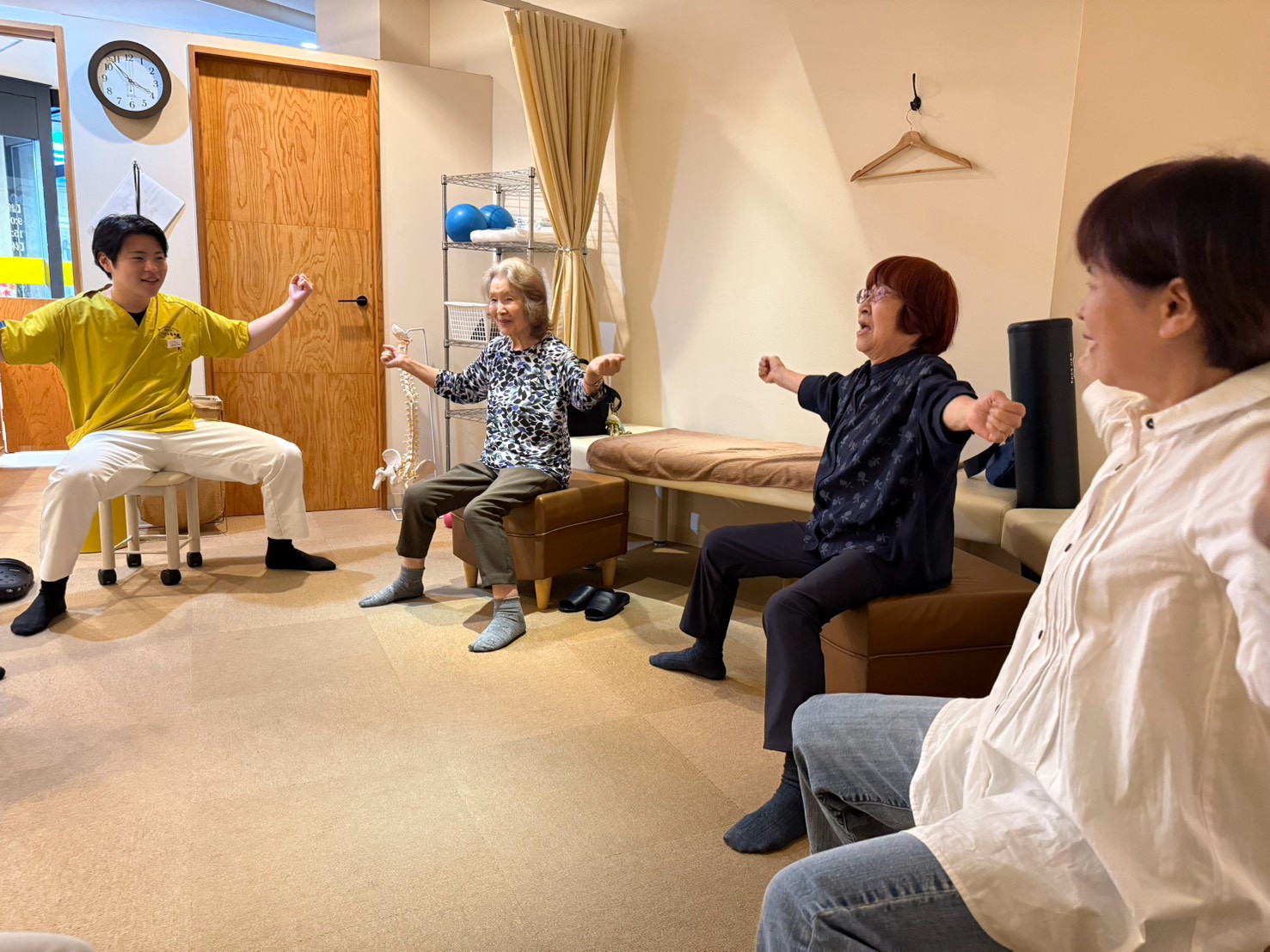体操教室で、参加者が笑顔で両腕を広げる体操をしている様子